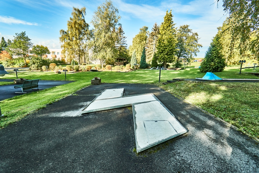 Minigolfbahn im Zickzack eingerahmt von einer Wiese umgeben von Bäumen unter blauen Himmel 