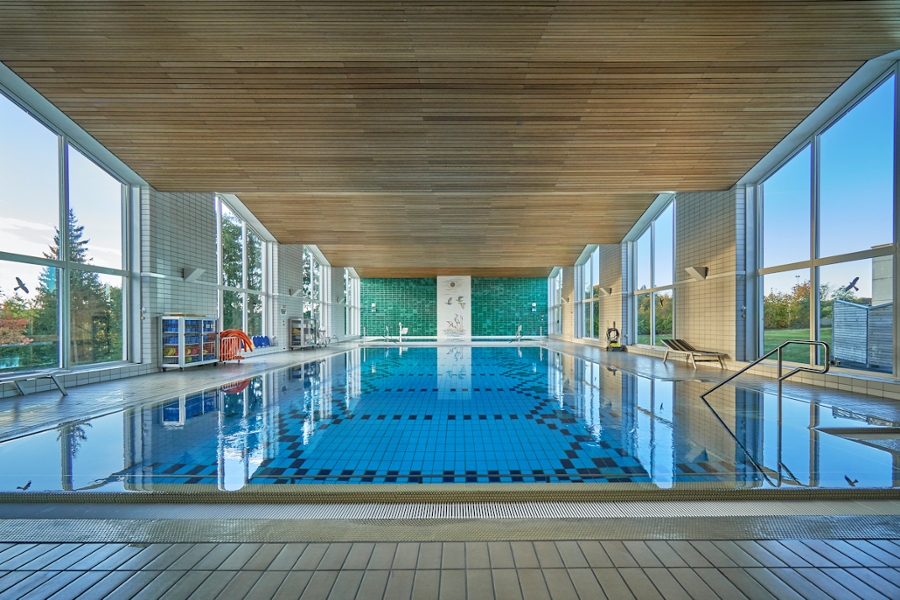 Lichtdurchflutetes Schwimmbad mit Holzdecke und Ausblick zu beiden Seiten in die Natur